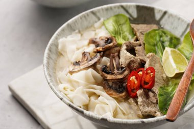 Pho Bo Vietnam çorbası sığır eti, pirinç eriştesi, pak choi ve mantarlar mermer tahtada gri bir kasede, fıstık, soya sosu, kırmızı biber