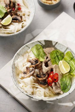 Pho Bo Vietnam çorbası sığır eti, pirinç eriştesi, pak choi ve mantarlar mermer tahtada gri bir kasede, fıstık, soya sosu, kırmızı biber