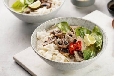 Pho Bo Vietnam çorbası sığır eti, pirinç eriştesi, pak choi ve mantarlar mermer tahtada gri bir kasede, fıstık, soya sosu, kırmızı biber