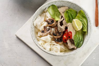 Pho Bo Vietnam çorbası sığır eti, pirinç eriştesi, pak choi ve mantarlar mermer tahtada gri bir kasede, fıstık, soya sosu, kırmızı biber