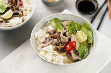 Pho Bo Vietnam çorbası sığır eti, pirinç eriştesi, pak choi ve mantarlar mermer tahtada gri bir kasede, fıstık, soya sosu, kırmızı biber