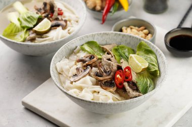 Pho Bo Vietnam çorbası sığır eti, pirinç eriştesi, pak choi ve mantarlar mermer tahtada gri bir kasede, fıstık, soya sosu, kırmızı biber