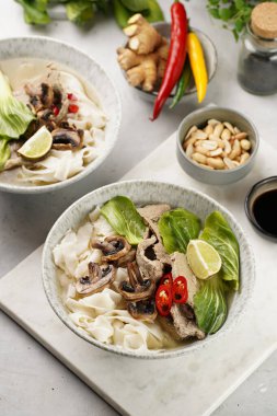 Pho Bo Vietnam çorbası sığır eti, pirinç eriştesi, pak choi ve mantarlar mermer tahtada gri bir kasede, fıstık, soya sosu, kırmızı biber