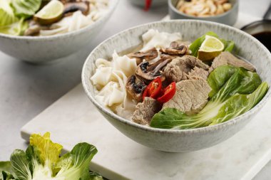 Pho Bo Vietnam çorbası sığır eti, pirinç eriştesi, pak choi ve mantarlar mermer tahtada gri bir kasede, fıstık, soya sosu, kırmızı biber