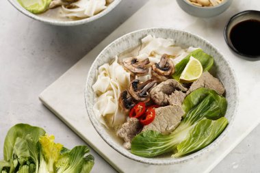 Pho Bo Vietnam çorbası sığır eti, pirinç eriştesi, pak choi ve mantarlar mermer tahtada gri bir kasede, fıstık, soya sosu, kırmızı biber