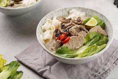 Pho Bo Vietnam çorbası sığır eti, pirinç eriştesi, pak choi ve mantarlar gri bir kasede peçete, fıstık, soya sosu, kırmızı biber