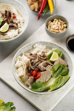 Pho Bo Vietnam çorbası sığır eti, pirinç eriştesi, pak choi ve mantarlar mermer tahtada gri bir kasede, fıstık, soya sosu, kırmızı biber