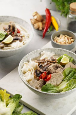 Pho Bo Vietnam çorbası sığır eti, pirinç eriştesi, pak choi ve mantarlar mermer tahtada gri bir kasede, fıstık, soya sosu, kırmızı biber