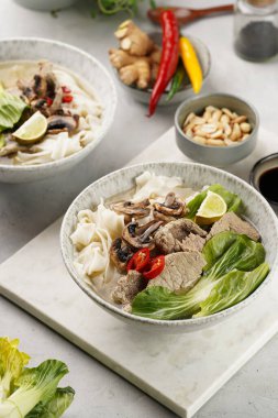 Pho Bo Vietnam çorbası sığır eti, pirinç eriştesi, pak choi ve mantarlar mermer tahtada gri bir kasede, fıstık, soya sosu, kırmızı biber