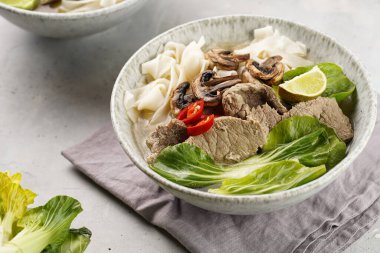 Pho Bo Vietnam çorbası sığır eti, pirinç eriştesi, pak choi ve mantarlar gri bir kasede peçete, fıstık, soya sosu, kırmızı biber