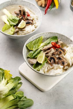 Pho Bo Vietnam çorbası sığır eti, pirinç eriştesi, pak choi ve mantarlar mermer tahtada gri bir kasede, fıstık, soya sosu, kırmızı biber