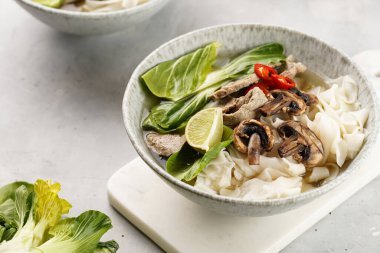 Pho Bo Vietnam çorbası sığır eti, pirinç eriştesi, pak choi ve mantarlar mermer tahtada gri bir kasede, fıstık, soya sosu, kırmızı biber