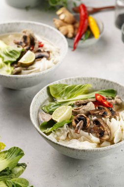 Pho Bo Vietnam çorbası sığır eti, pirinç eriştesi, Çin mantısı ve mantarlar gri bir kasede, fıstık, soya sosu, kırmızı biber