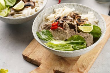 Pho Bo Vietnam çorbası sığır eti, pirinç eriştesi, pak choi ve mantarlar tahta tahtada gri bir kasede, fıstık, soya sosu, kırmızı biber