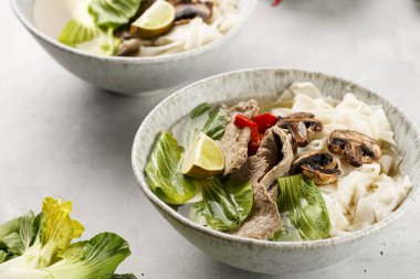 Pho Bo Vietnam çorbası sığır eti, pirinç eriştesi, Çin mantısı ve mantarlar gri bir kasede, fıstık, soya sosu, kırmızı biber