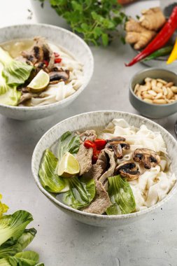 Pho Bo Vietnam çorbası sığır eti, pirinç eriştesi, Çin mantısı ve mantarlar gri bir kasede, fıstık, soya sosu, kırmızı biber