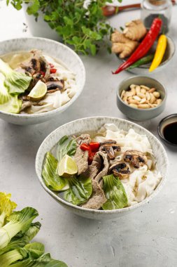 Pho Bo Vietnam çorbası sığır eti, pirinç eriştesi, Çin mantısı ve mantarlar gri bir kasede, fıstık, soya sosu, kırmızı biber