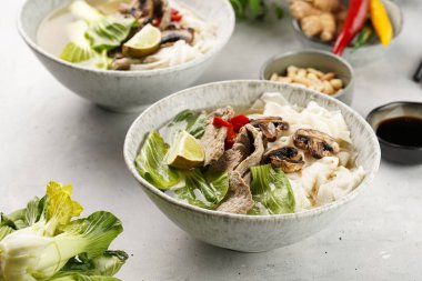 Pho Bo Vietnam çorbası sığır eti, pirinç eriştesi, Çin mantısı ve mantarlar gri bir kasede, fıstık, soya sosu, kırmızı biber