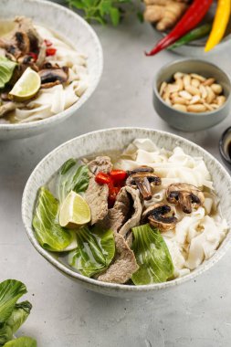 Pho Bo Vietnam çorbası sığır eti, pirinç eriştesi, Çin mantısı ve mantarlar gri bir kasede, fıstık, soya sosu, kırmızı biber