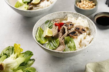 Pho Bo Vietnam çorbası sığır eti, pirinç eriştesi, Çin mantısı ve mantarlar gri bir kasede, fıstık, soya sosu, kırmızı biber