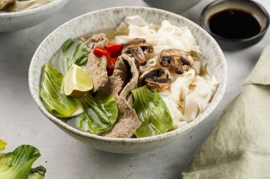 Pho Bo Vietnam çorbası sığır eti, pirinç eriştesi, Çin mantısı ve mantarlar gri bir kasede, fıstık, soya sosu, kırmızı biber