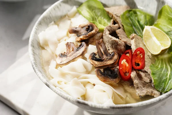 Pho Bo Vietnam çorbası sığır eti, pirinç eriştesi, pak choi ve mantarlar mermer tahtada gri bir kasede, fıstık, soya sosu, kırmızı biber