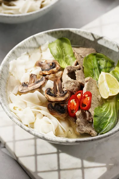 Pho Bo Vietnam çorbası sığır eti, pirinç eriştesi, pak choi ve mantarlar mermer tahtada gri bir kasede, fıstık, soya sosu, kırmızı biber