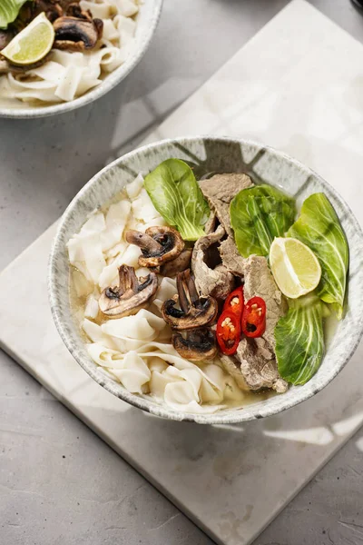 Pho Bo Vietnam çorbası sığır eti, pirinç eriştesi, pak choi ve mantarlar mermer tahtada gri bir kasede, fıstık, soya sosu, kırmızı biber