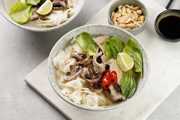 Pho Bo Vietnam çorbası sığır eti, pirinç eriştesi, pak choi ve mantarlar mermer tahtada gri bir kasede, fıstık, soya sosu, kırmızı biber