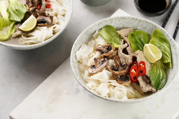 Pho Bo Vietnam çorbası sığır eti, pirinç eriştesi, pak choi ve mantarlar mermer tahtada gri bir kasede, fıstık, soya sosu, kırmızı biber