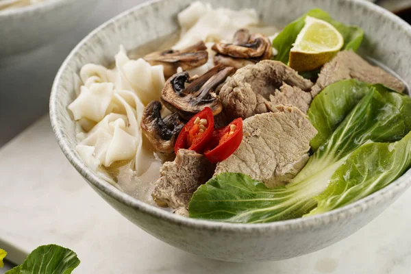 Pho Bo Vietnam çorbası sığır eti, pirinç eriştesi, pak choi ve mantarlar mermer tahtada gri bir kasede, fıstık, soya sosu, kırmızı biber