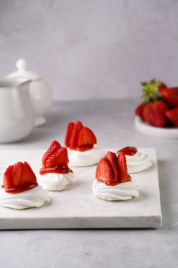 Taze çilek ve kırmızı reçelli mini pavlova. Mermer tahtada, beyaz arka planda lezzetli kremalı pastalar.