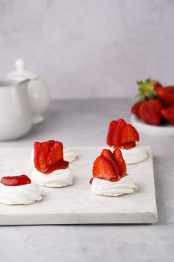 Taze çilek ve kırmızı reçelli mini pavlova. Mermer tahtada, beyaz arka planda lezzetli kremalı pastalar.