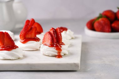 Taze çilek ve kırmızı reçelli mini pavlova. Mermer tahtada, beyaz arka planda lezzetli kremalı pastalar.