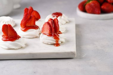Taze çilek ve kırmızı reçelli mini pavlova. Mermer tahtada, beyaz arka planda lezzetli kremalı pastalar.