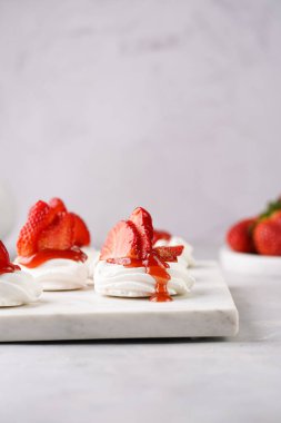 Taze çilek ve kırmızı reçelli mini pavlova. Mermer tahtada, beyaz arka planda lezzetli kremalı pastalar.