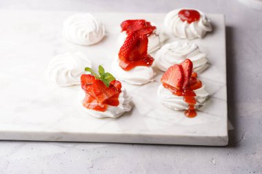 Taze çilek ve kırmızı reçelli mini pavlova. Mermer tahtada, beyaz arka planda lezzetli kremalı pastalar.