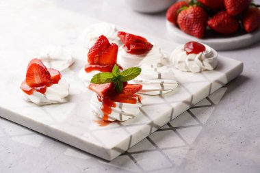 Taze çilek ve kırmızı reçelli mini pavlova. Mermer tahtada, beyaz arka planda lezzetli kremalı pastalar.