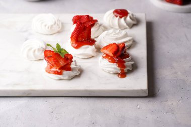 Taze çilek ve kırmızı reçelli mini pavlova. Mermer tahtada, beyaz arka planda lezzetli kremalı pastalar.