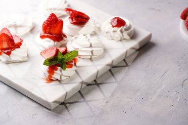 Taze çilek ve kırmızı reçelli mini pavlova. Mermer tahtada, beyaz arka planda lezzetli kremalı pastalar.