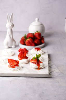Taze çilek ve kırmızı reçelli mini pavlova. Beyaz arkaplanda mermer tahtada lezzetli kremalı pastalar. Paskalya tavşanı.