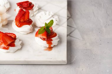 Taze çilek ve kırmızı reçelli mini pavlova. Mermer tahtada, beyaz arka planda lezzetli kremalı pastalar.