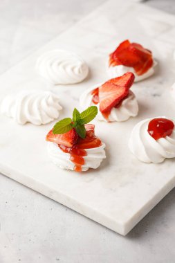 Taze çilek ve kırmızı reçelli mini pavlova. Mermer tahtada, beyaz arka planda lezzetli kremalı pastalar.