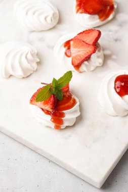 Taze çilek ve kırmızı reçelli mini pavlova. Mermer tahtada, beyaz arka planda lezzetli kremalı pastalar.