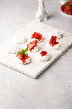 Taze çilek ve kırmızı reçelli mini pavlova. Mermer tahtada, beyaz arka planda lezzetli kremalı pastalar.