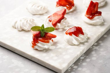 Taze çilek ve kırmızı reçelli mini pavlova. Mermer tahtada, beyaz arka planda lezzetli kremalı pastalar.