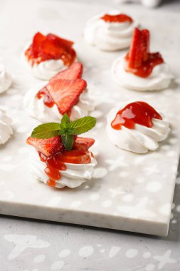 Taze çilek ve kırmızı reçelli mini pavlova. Mermer tahtada, beyaz arka planda lezzetli kremalı pastalar.