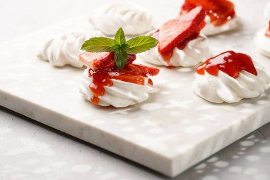 Taze çilek ve kırmızı reçelli mini pavlova. Mermer tahtada, beyaz arka planda lezzetli kremalı pastalar.