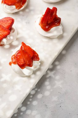 Taze çilek ve kırmızı reçelli mini pavlova. Mermer tahtada, beyaz arka planda lezzetli kremalı pastalar.