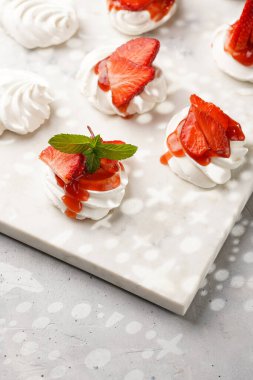 Taze çilek ve kırmızı reçelli mini pavlova. Mermer tahtada, beyaz arka planda lezzetli kremalı pastalar.
